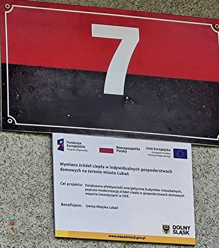 numer domu "7" uieszczony na czerwono-czaarnym tle, poniżej tabliczka informująca o projekcie