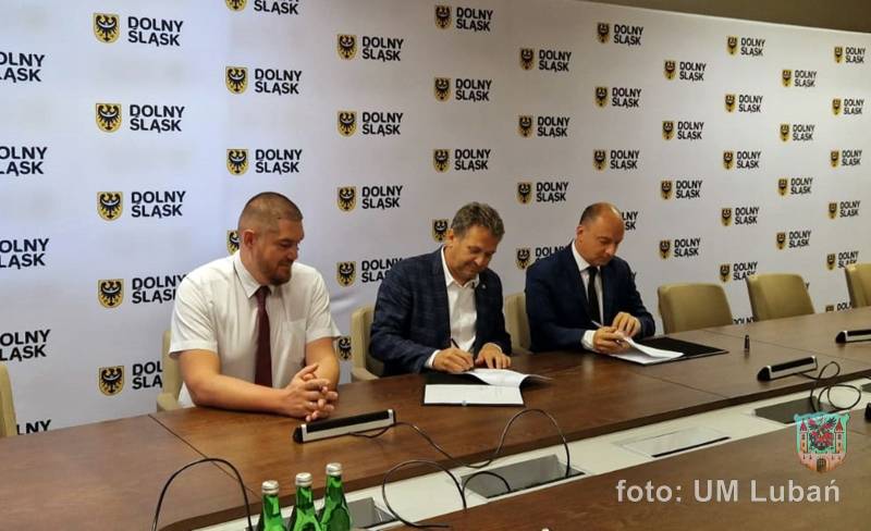 trzech mężczyzn siedzących przy stole, podpisują dokumenty