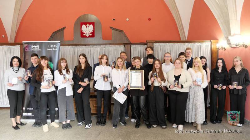 zdjęcie grupowe - młodzież na tle baneru z kolorowym minerałem, nad nimi wisi godło Polski